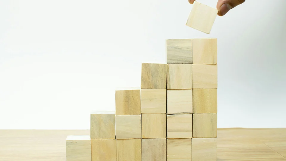 building blocks stacked to look like a staircase with a hand putting the last block on top