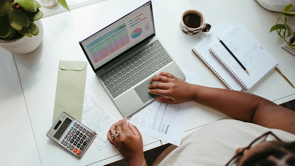 Woman reviewing graphs and statements at a desk with paperwork and calculator