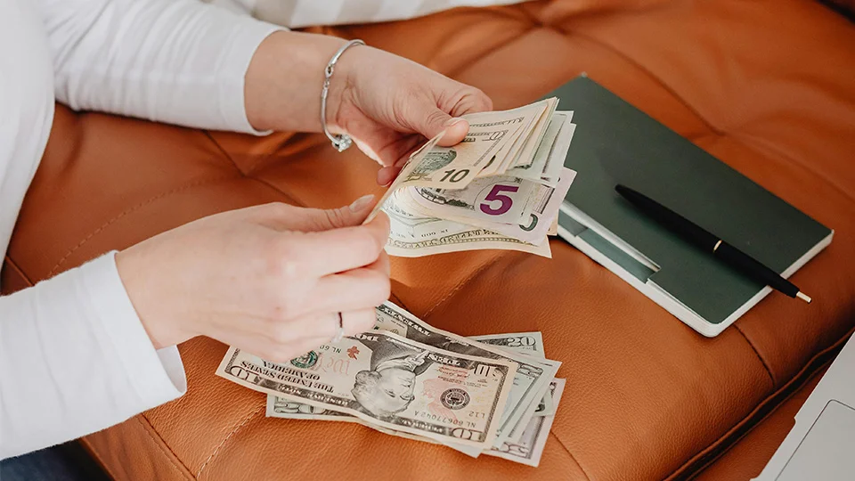Person counting money next to a ledger